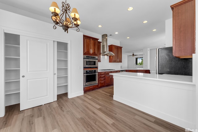 kitchen with wall chimney exhaust hood, kitchen peninsula, pendant lighting, light hardwood / wood-style floors, and appliances with stainless steel finishes