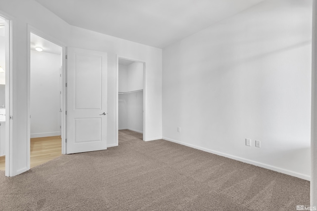 unfurnished bedroom featuring a walk in closet, light carpet, and a closet