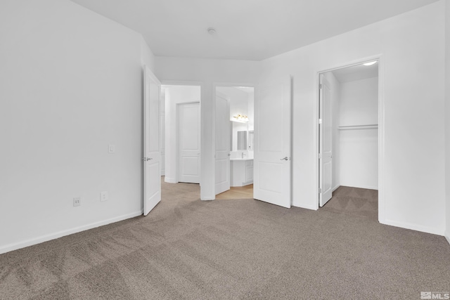 unfurnished bedroom with a spacious closet, a closet, carpet floors, and ensuite bath