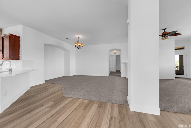 unfurnished living room featuring sink, light hardwood / wood-style floors, and ceiling fan with notable chandelier