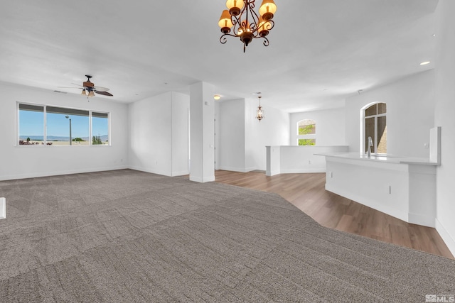 unfurnished living room with light hardwood / wood-style flooring, a healthy amount of sunlight, and ceiling fan with notable chandelier