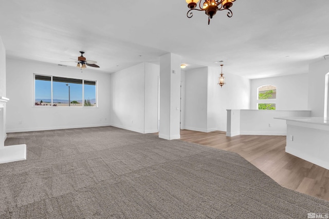 unfurnished living room featuring ceiling fan with notable chandelier and light wood-type flooring