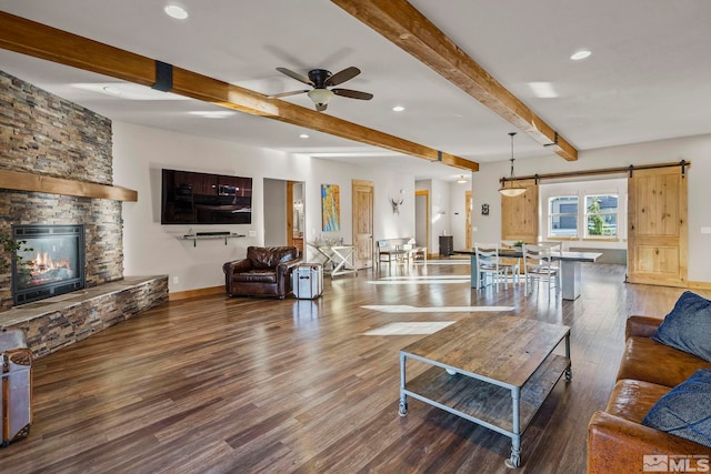 living room featuring dark hardwood / wood-style flooring, ceiling fan, beam ceiling, a barn door, and a fireplace