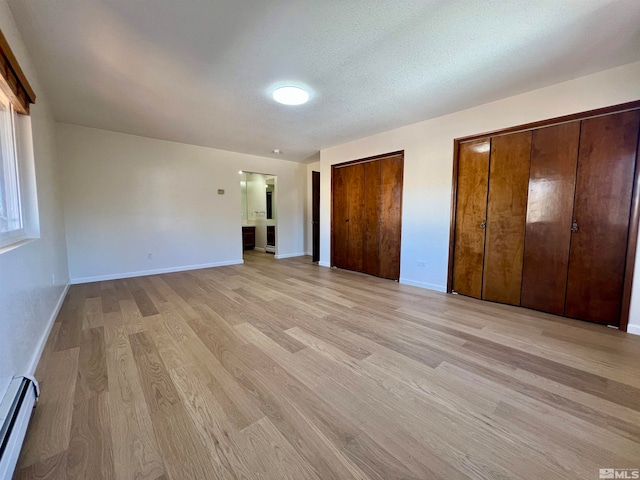 unfurnished bedroom with multiple closets, a baseboard radiator, a textured ceiling, and light hardwood / wood-style floors