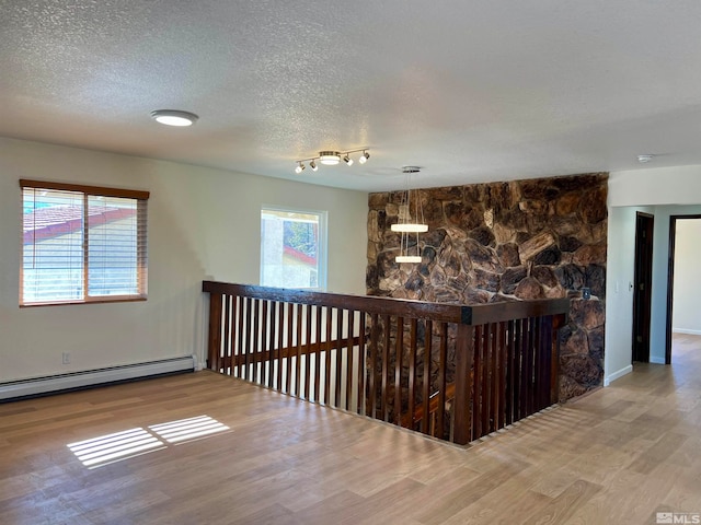 hallway featuring baseboard heating, a wealth of natural light, hardwood / wood-style floors, and a textured ceiling