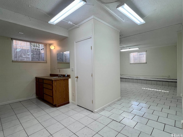 basement featuring a healthy amount of sunlight, sink, a textured ceiling, and light tile patterned flooring