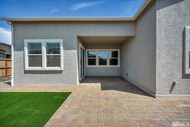 property entrance featuring a patio, stucco siding, and fence