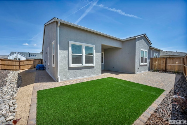 rear view of house featuring stucco siding, a patio area, a yard, and a fenced backyard