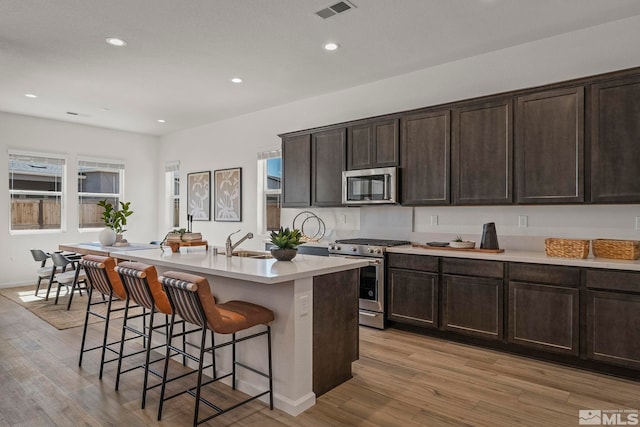 kitchen with sink, stainless steel appliances, an island with sink, a breakfast bar, and light wood-type flooring