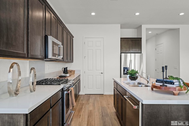 kitchen featuring sink, light hardwood / wood-style flooring, an island with sink, appliances with stainless steel finishes, and dark brown cabinets