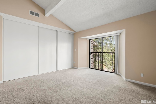 carpeted empty room featuring lofted ceiling with beams and a textured ceiling