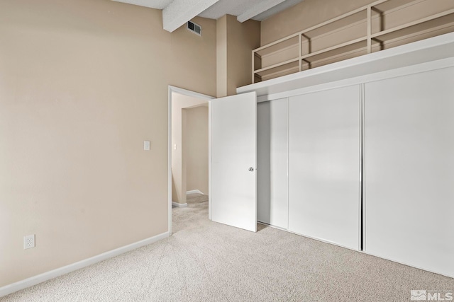 unfurnished bedroom featuring beam ceiling, a closet, and light colored carpet