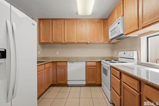 kitchen with light tile patterned floors, white appliances, light stone counters, and sink