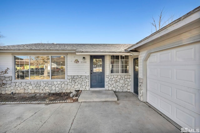 view of exterior entry with a garage, stone siding, and roof with shingles