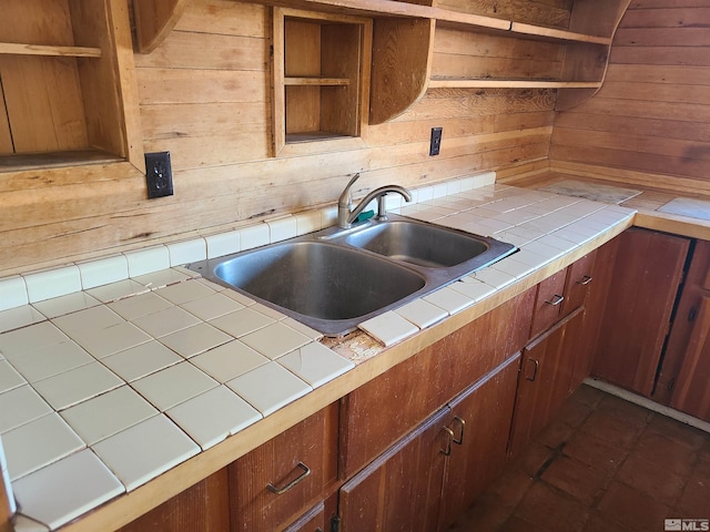 kitchen featuring tile countertops, wood walls, sink, and dark tile patterned flooring