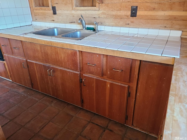 kitchen featuring backsplash, tile countertops, wooden walls, and sink