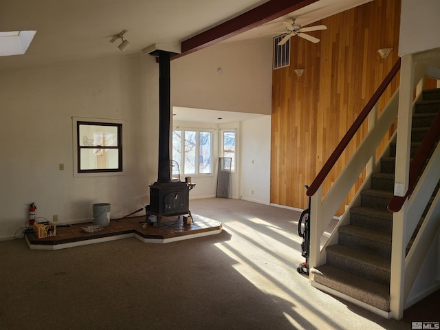 unfurnished living room featuring a wood stove, ceiling fan, beamed ceiling, high vaulted ceiling, and wood walls