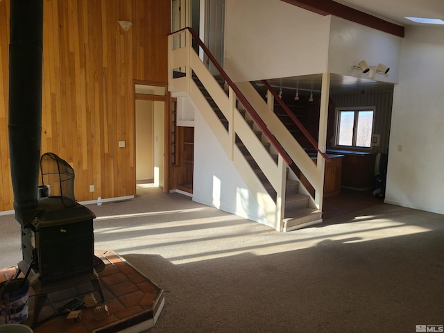 unfurnished living room featuring wood walls, a wood stove, high vaulted ceiling, carpet flooring, and beamed ceiling