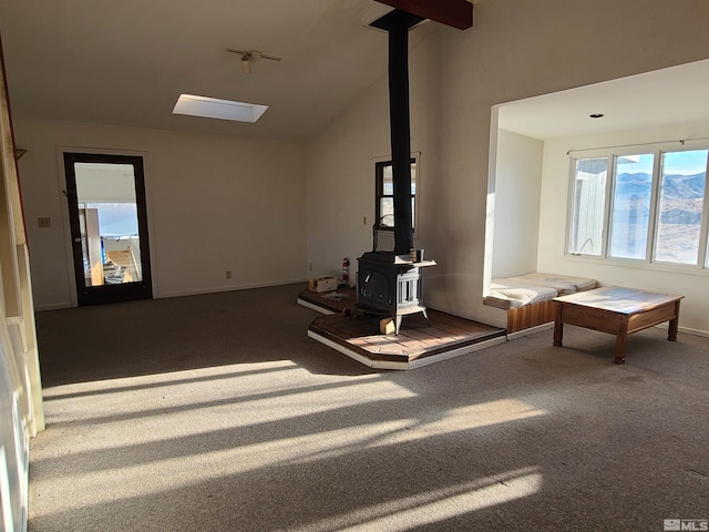 unfurnished living room featuring a wood stove, carpet floors, a skylight, and high vaulted ceiling