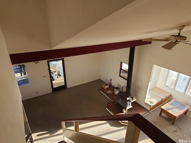 unfurnished living room with dark carpet, a wood stove, and ceiling fan