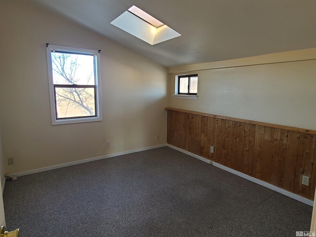 bonus room with wood walls, vaulted ceiling with skylight, and plenty of natural light