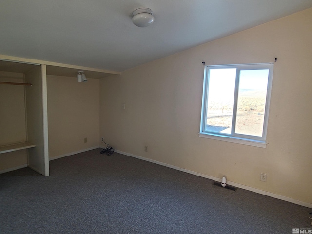 unfurnished bedroom featuring a closet, lofted ceiling, and dark colored carpet