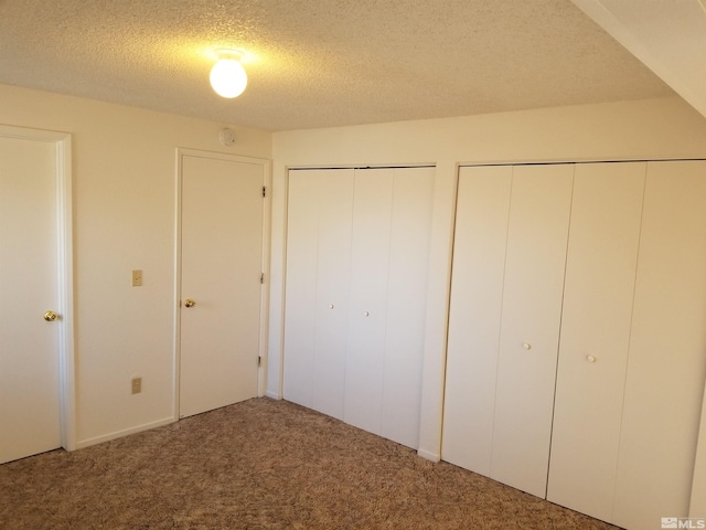 unfurnished bedroom with a textured ceiling, carpet floors, and multiple closets