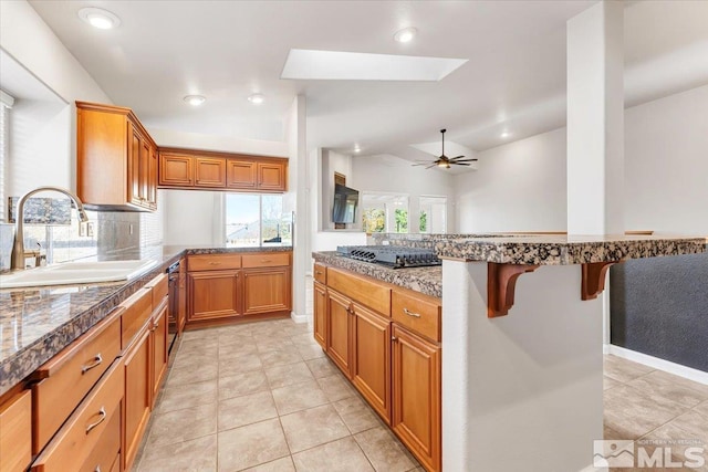 kitchen featuring black gas stovetop, sink, a skylight, ceiling fan, and a kitchen bar