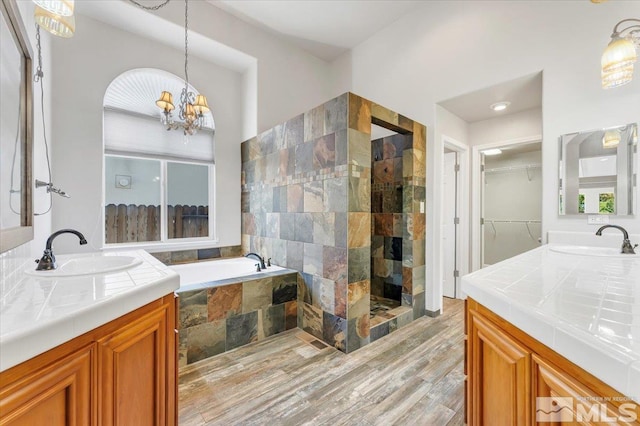 bathroom with hardwood / wood-style flooring, a notable chandelier, plus walk in shower, and vanity