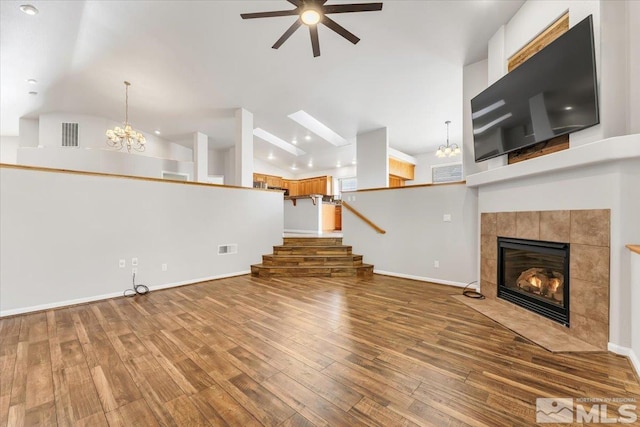 unfurnished living room with hardwood / wood-style floors, ceiling fan with notable chandelier, a tile fireplace, and vaulted ceiling