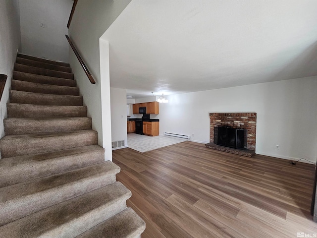 unfurnished living room with baseboard heating, hardwood / wood-style floors, an inviting chandelier, and a brick fireplace