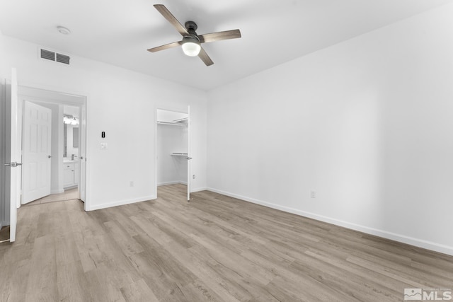 unfurnished bedroom with a closet, a spacious closet, light hardwood / wood-style flooring, and ceiling fan