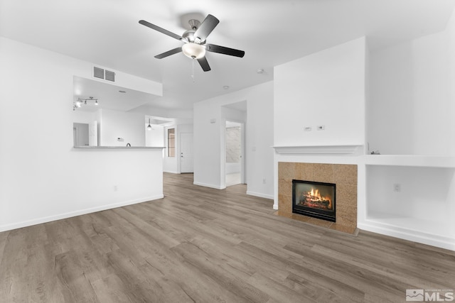 unfurnished living room featuring ceiling fan, wood-type flooring, and a tile fireplace