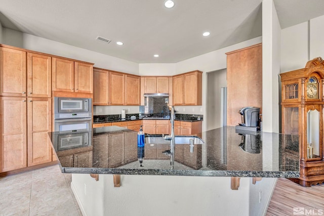 kitchen with sink, a kitchen breakfast bar, dark stone countertops, and stainless steel appliances