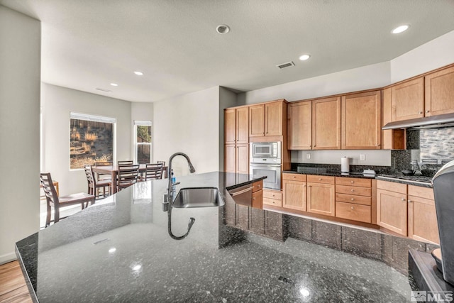 kitchen featuring appliances with stainless steel finishes, an island with sink, dark stone counters, and sink