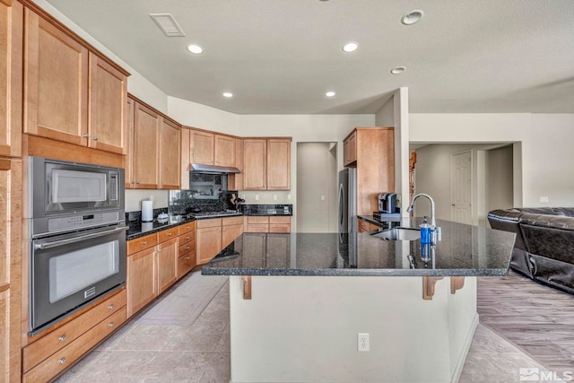 kitchen featuring sink, a breakfast bar area, dark stone countertops, light wood-type flooring, and stainless steel appliances