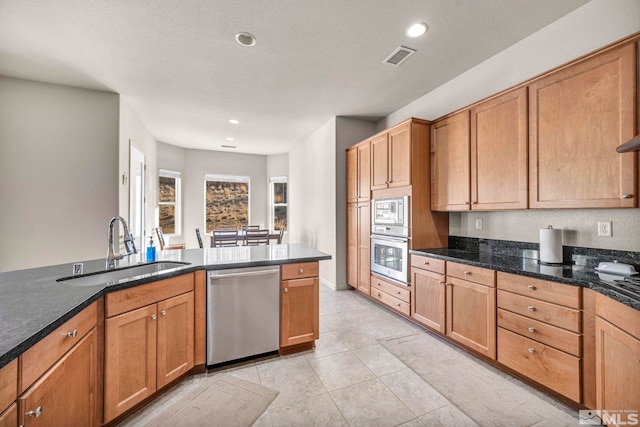 kitchen with sink, dark stone countertops, light tile patterned floors, a textured ceiling, and stainless steel appliances