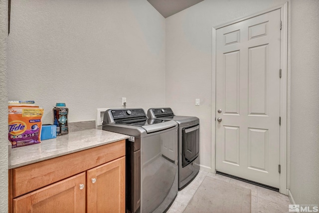 clothes washing area with cabinets, washing machine and dryer, and light tile patterned floors