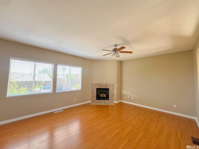 unfurnished living room featuring a tile fireplace, ceiling fan, and light hardwood / wood-style flooring