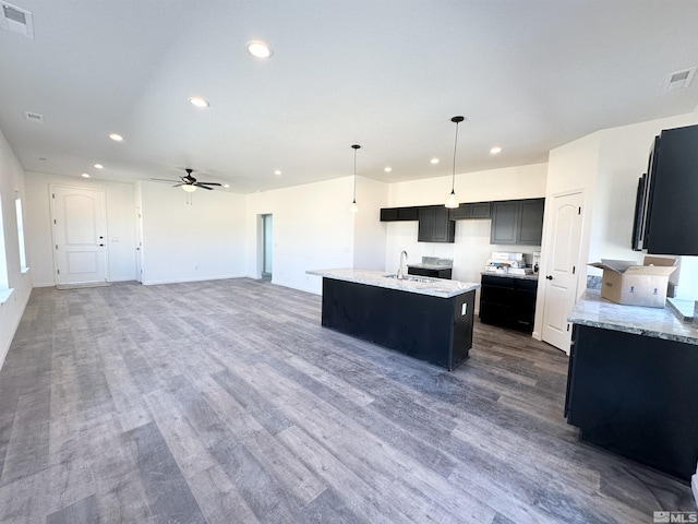 kitchen with ceiling fan, a kitchen island with sink, dark wood-type flooring, sink, and decorative light fixtures