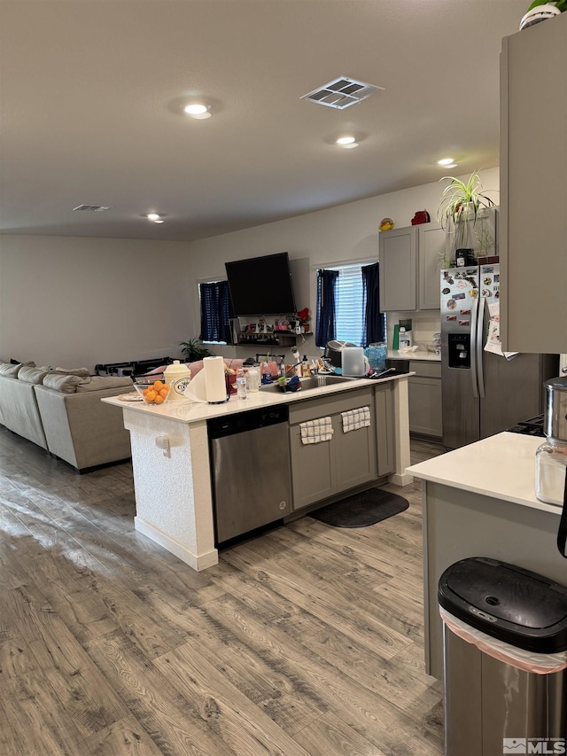 kitchen featuring hardwood / wood-style floors, a center island, stainless steel appliances, and gray cabinets