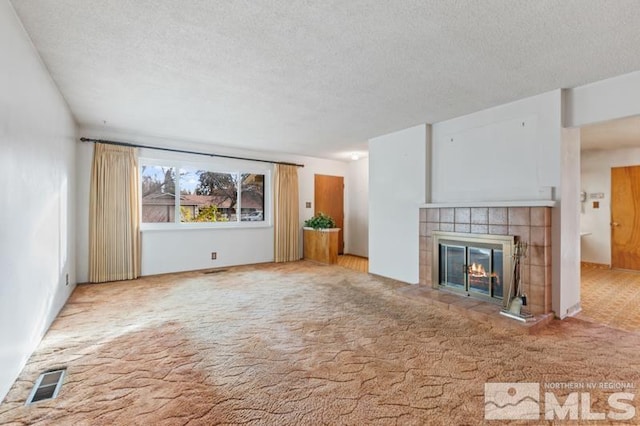 unfurnished living room with a textured ceiling, light colored carpet, and a tiled fireplace