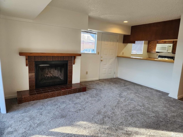 unfurnished living room featuring dark colored carpet, a textured ceiling, and a tile fireplace