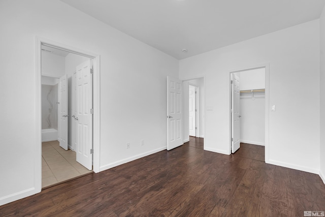 unfurnished bedroom with a closet, connected bathroom, a walk in closet, and dark hardwood / wood-style flooring