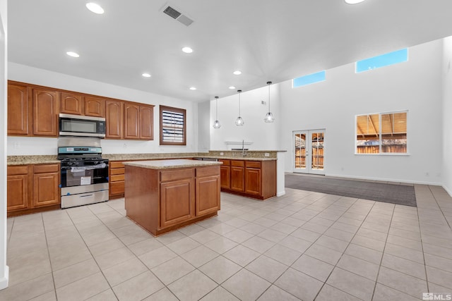 kitchen with appliances with stainless steel finishes, light tile patterned floors, hanging light fixtures, and light stone counters