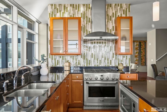 kitchen with dark stone counters, wall chimney exhaust hood, stainless steel appliances, sink, and pendant lighting