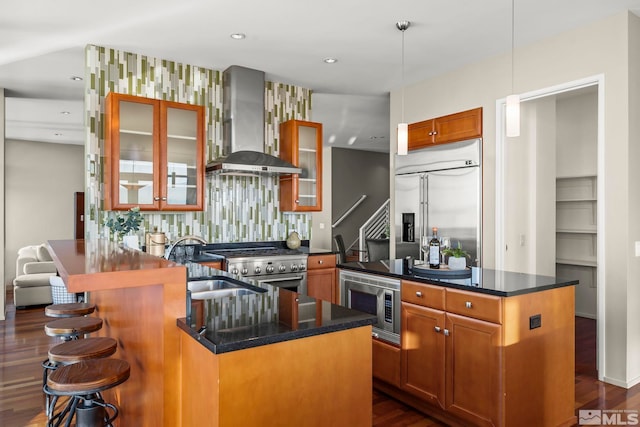 kitchen with dark hardwood / wood-style flooring, built in appliances, a center island, and wall chimney exhaust hood