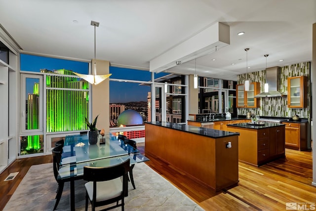 kitchen featuring a center island, sink, hanging light fixtures, wall chimney exhaust hood, and light hardwood / wood-style floors