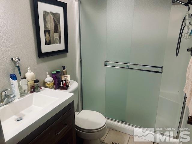 bathroom featuring tile patterned flooring, vanity, toilet, and a shower with door