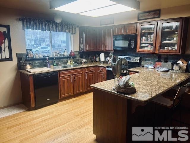 kitchen featuring black appliances, sink, light hardwood / wood-style floors, light stone counters, and kitchen peninsula